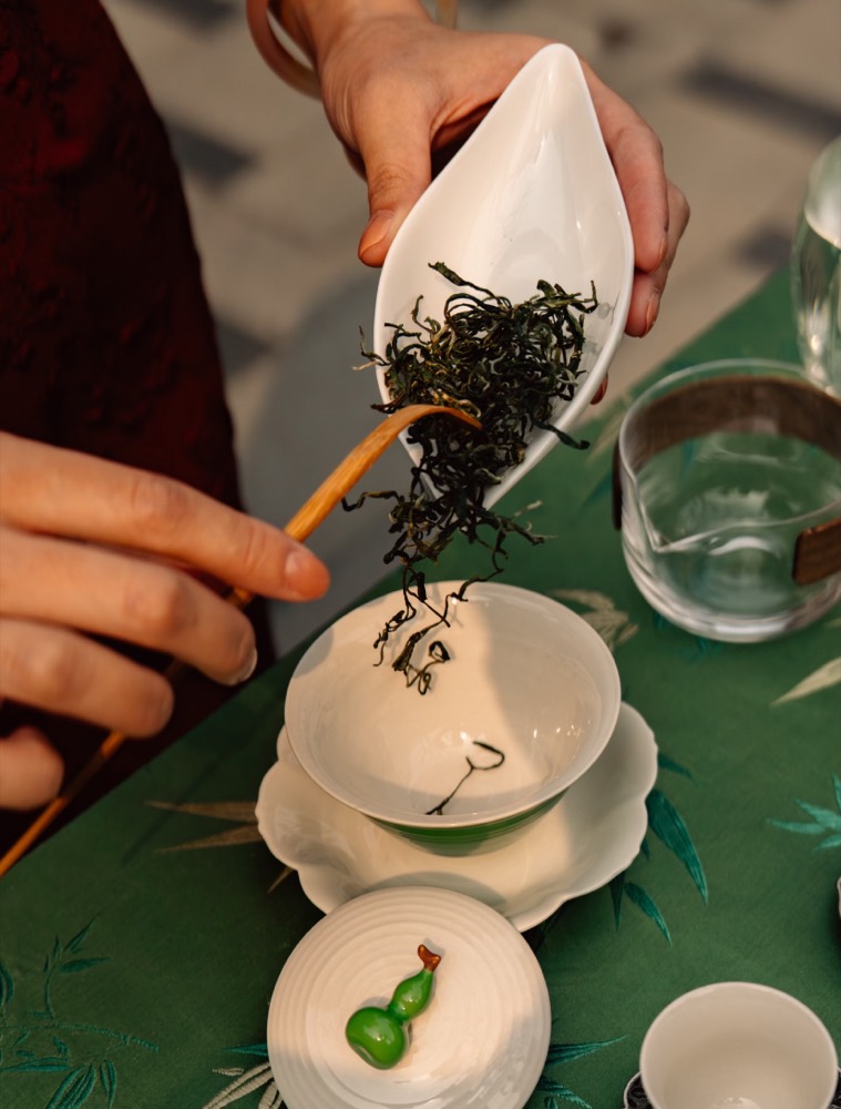 A traveler pouring fresh tea leaves into a gaiwan during a tea ceremony