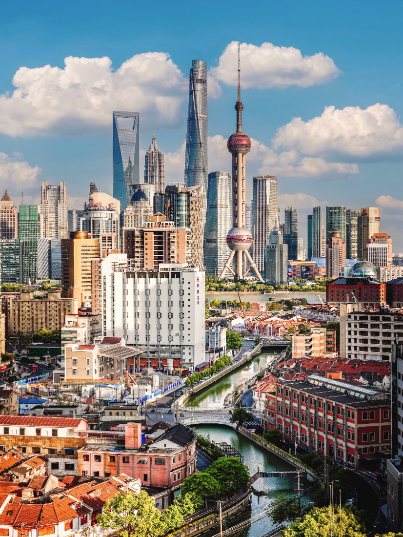 The modern Shanghai skyline rising above old lane houses and a canal