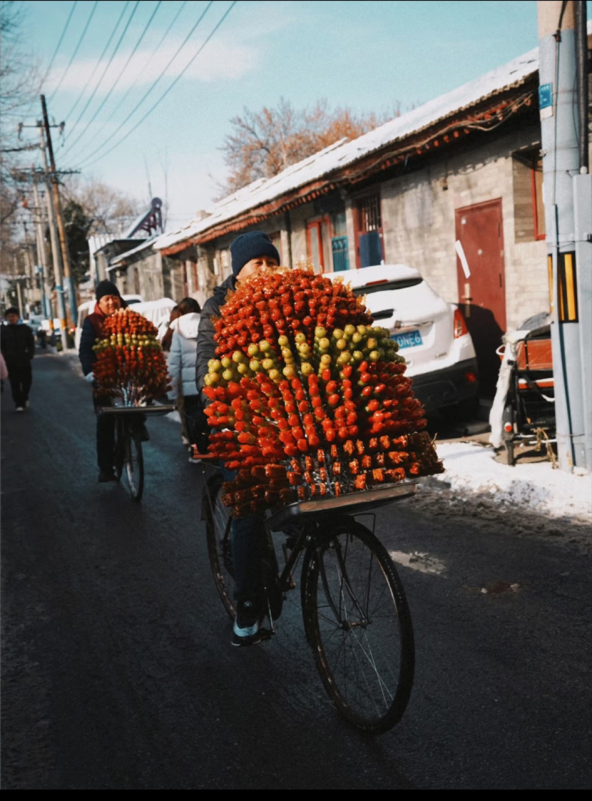 A winter Beijing hutong with vendors cycling past carrying persimmons and produce