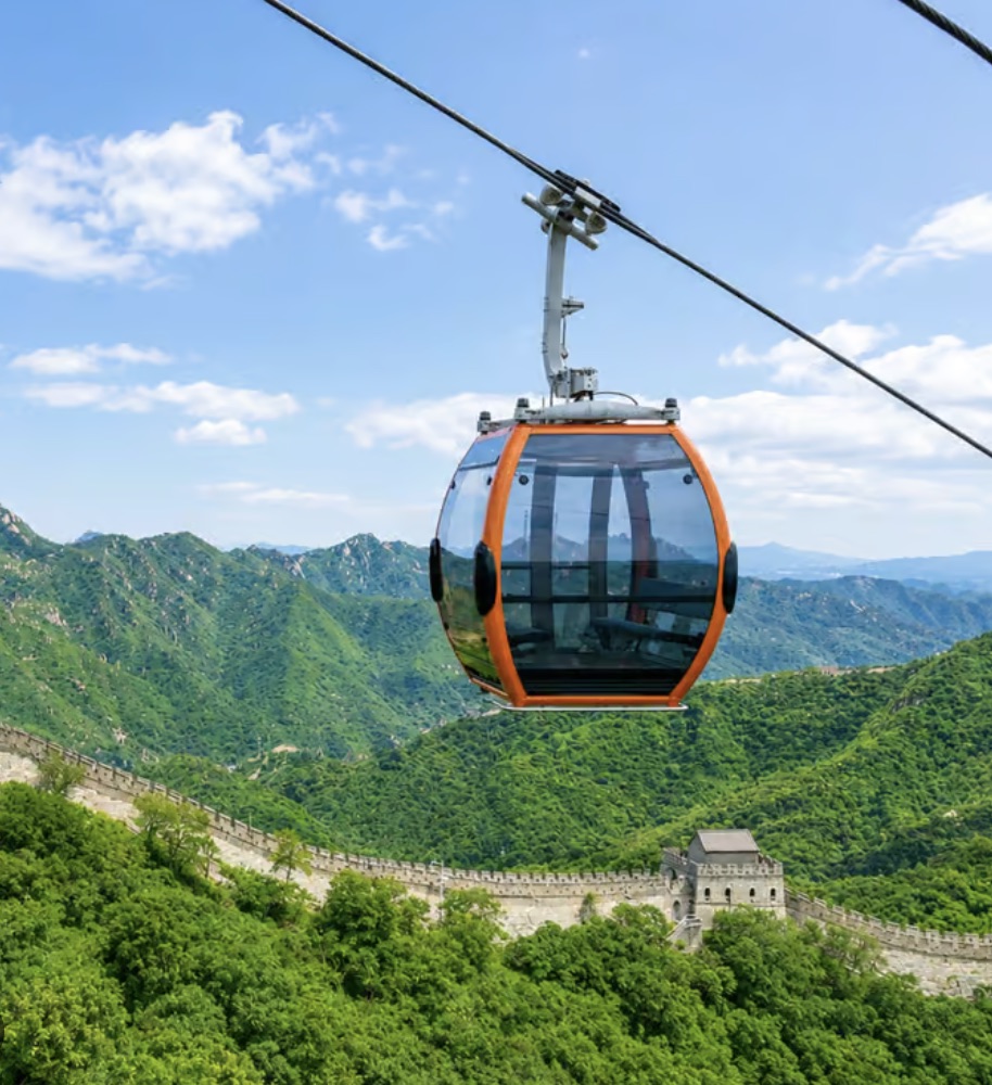A cable car rising toward the Great Wall over green mountains at Mutianyu