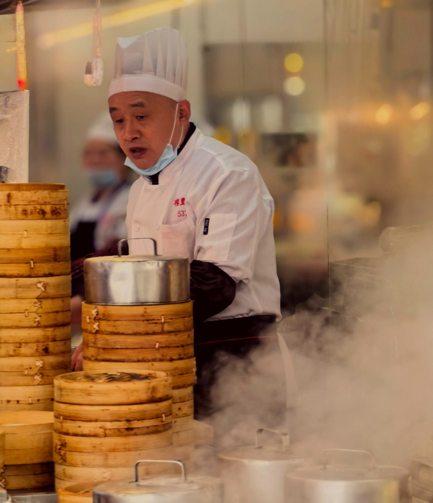 A dim sum chef lifting steaming bamboo baskets of Cantonese dumplings