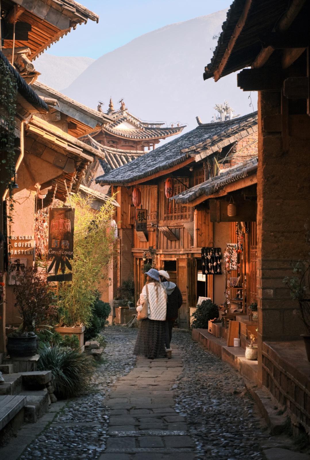 A lone figure walking a cobbled Yunnan old-town lane in golden evening light